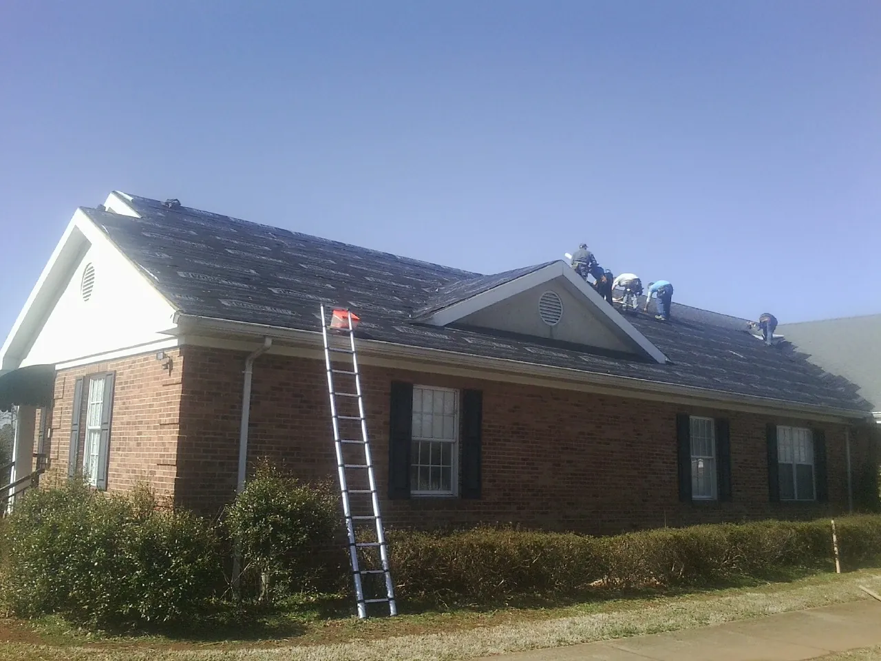 Crew tearing shingles off a brick ranch roof with a ladder set — Metal Roof Repair work by our crew in Burbank